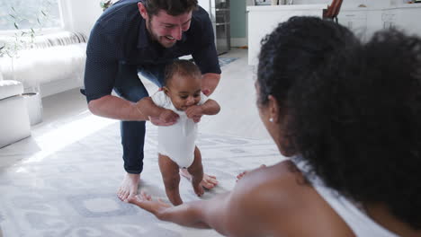 padres alentando a un bebé sonriente a dar los primeros pasos y caminar en casa