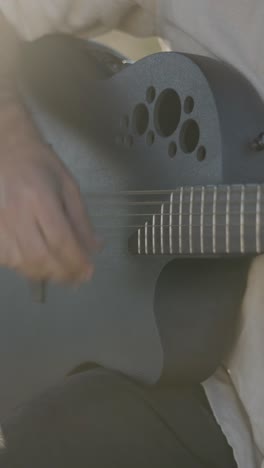 close-up of a hand playing a black acoustic-electric guitar