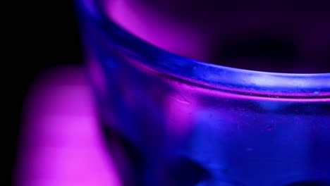 macro shot of the edge of a glass with the blue and violet lights of a party inside of a pub, close up view