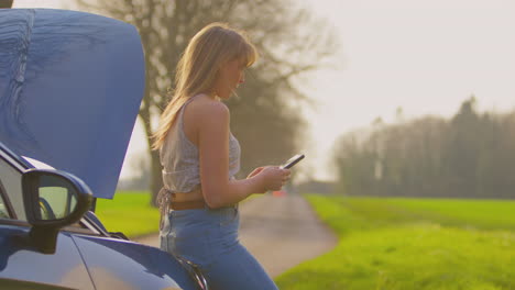 Mujer-Frustrada-Con-Un-Coche-Averiado-En-Una-Carretera-Rural-Pidiendo-Ayuda-Por-Teléfono-Móvil