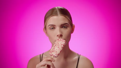 attractive young woman eats white berry popsicle, purple studio shot