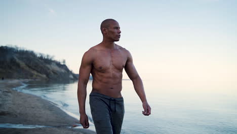 attractive and muscular man walking along the shore in slow motion