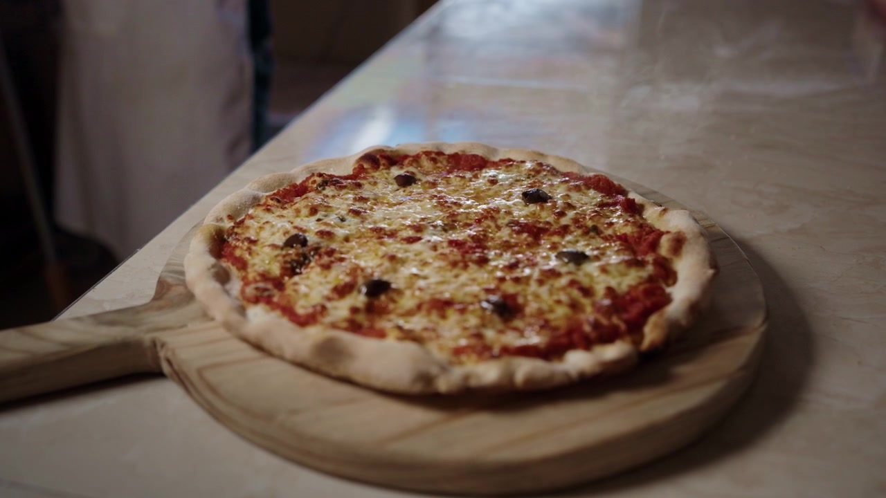 Pizza con olive e acciughe appena sfornata, posizionata su un piatto da portata in legno, primo piano.