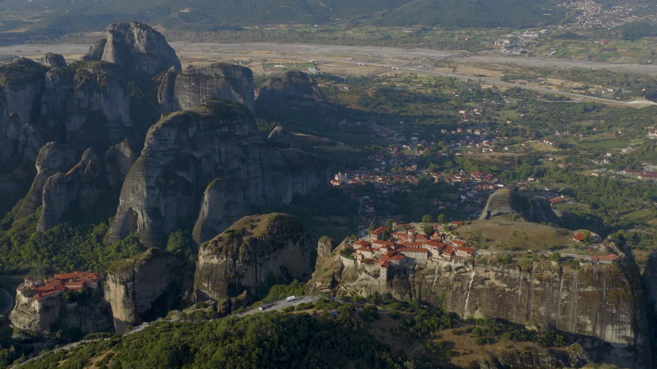 Cinematic aerial view of Meteora monastery in Greece perched on towering cliffs, dramatic rock formations and lush green valley create a breathtaking historic scene
