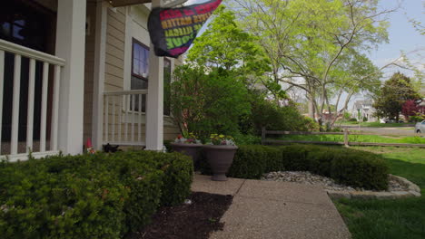 Push-towards-the-front-door-of-a-house-and-the-rainbow-flag-flying-off-the-porch-on-a-beautiful-spring-day-in-the-suburbs-with-a-boom-up-the-side-of-the-house-to-reveal-the-neighborhood-beyond