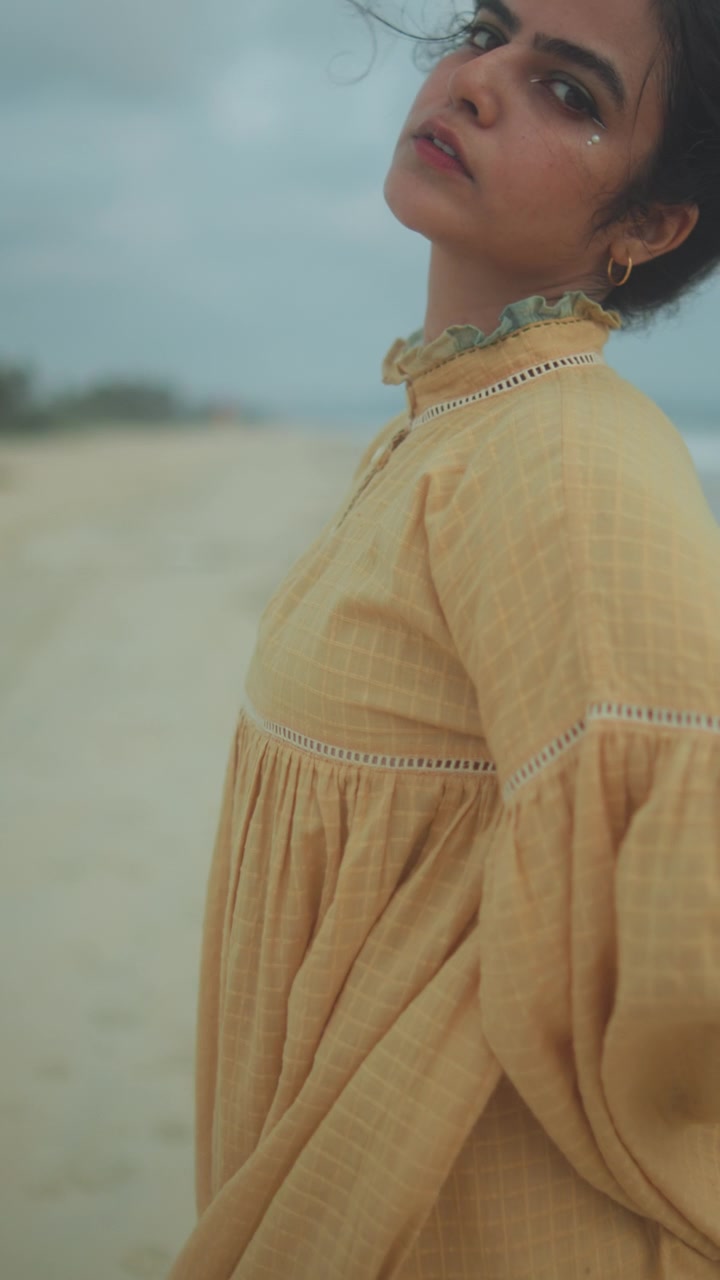 Young woman posing thoughtfully on a sandy beach in a flowing yellow dress, creating a dreamy cinematic portrait with soft natural light and shallow depth of field