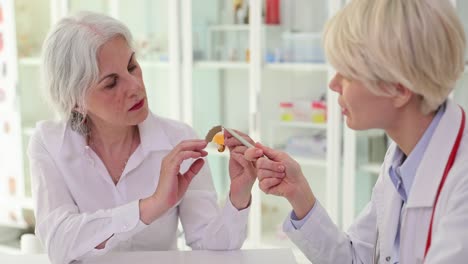 audiologist explaining a hearing aid to an elderly patient