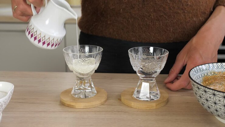 Woman pours milk from vintage jug in crystal glasses, preparing dalgona coffee