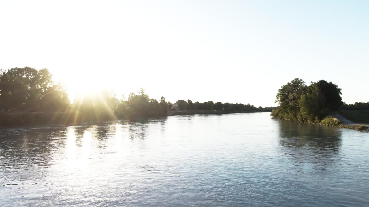 Aerial shot flying backwards over a river with beautifulflares from the sun during sunset.
