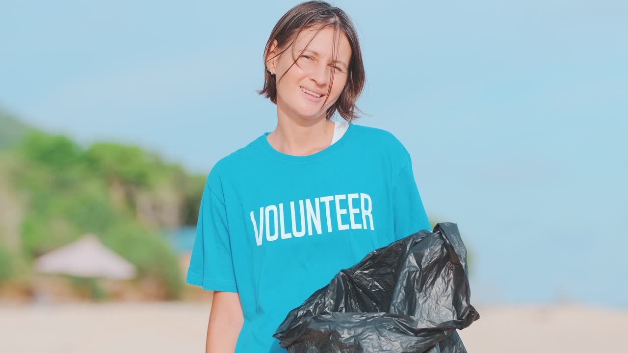 Young caring woman volunteer posing throwing plastic bottle in black bag