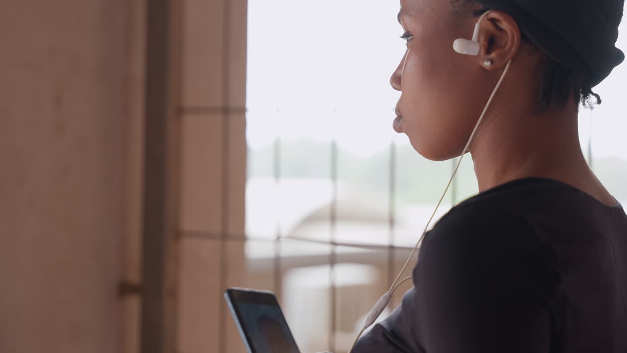 Creatore che esamina un dispositivo in controluce soffuso. Artista donna che studia la silhouette del telefono con gli auricolari. Designer donna che riflette su idee mentre è illuminata da una delicata luce dalla finestra con gli auricolari.