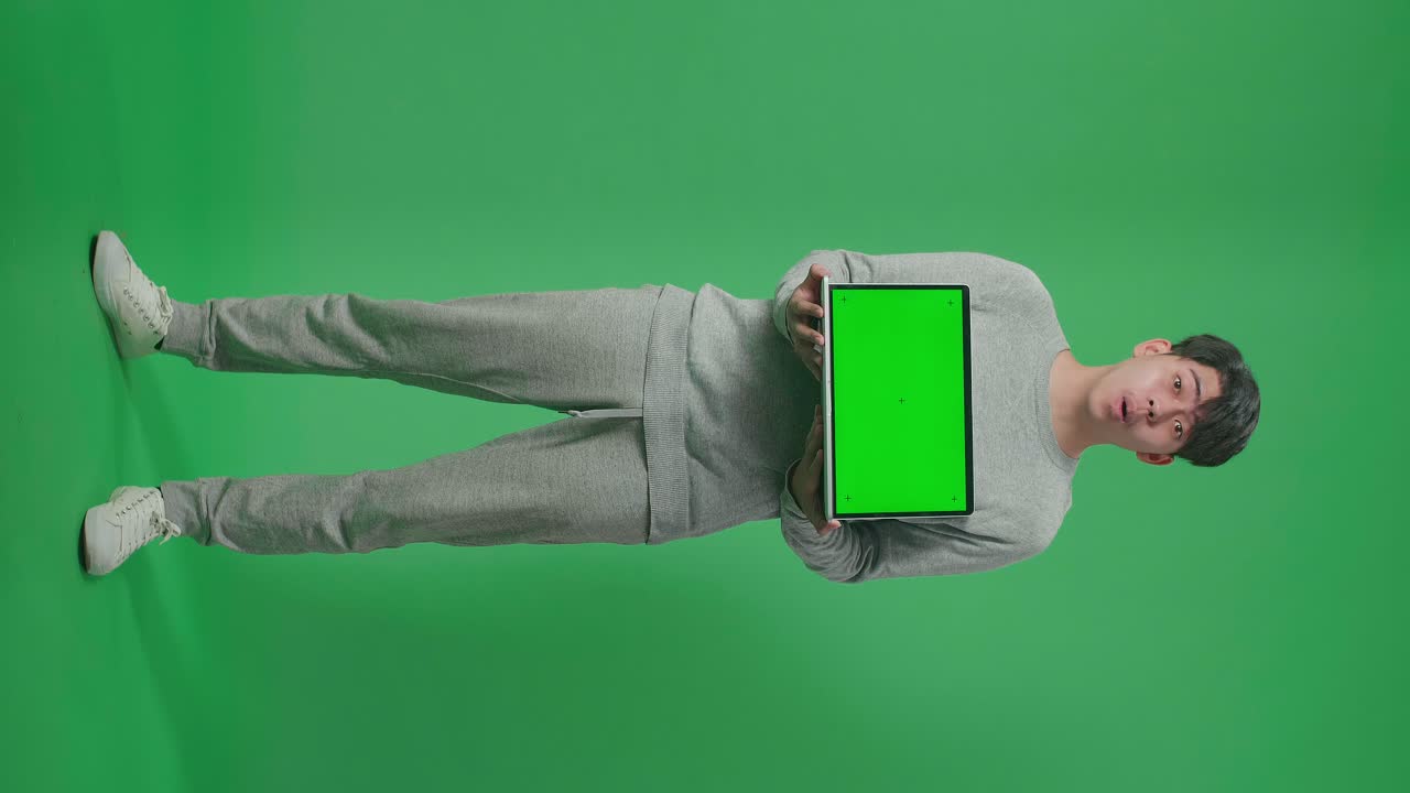 cuerpo lleno de hombre asiático sonriente diciendo wow mientras sostiene computadora de pantalla verde en el estudio de pantalla verde