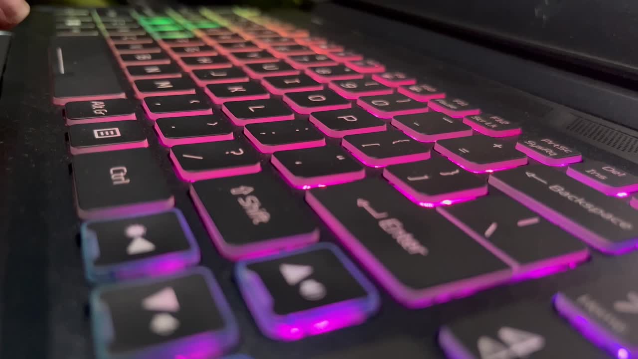 manos escribiendo en el teclado retroiluminado colorido del ordenador portátil