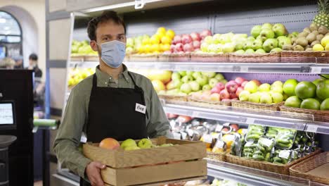 retrato de un hombre guapo con máscara facial y delantal de pie en una tienda de alimentos con una caja de frutas en el interior