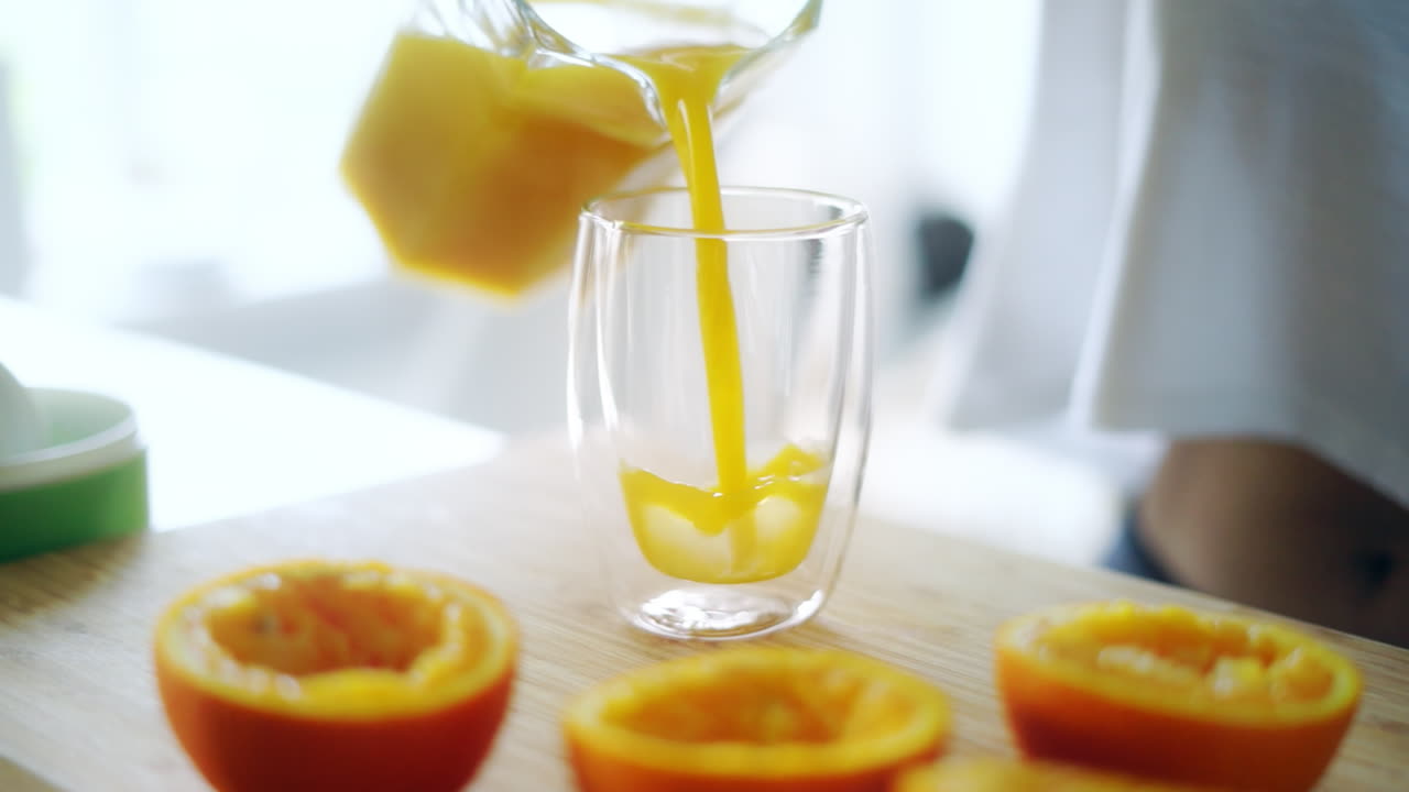 Versando succo d'arancia fresco da una brocca di vetro in un bicchiere. Arance spremute.