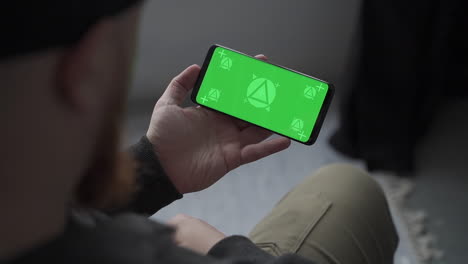 man holding smartphone with horizontal green screen chroma, reading, touching. mockup.