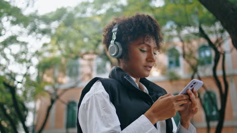 girl earphones using phone app to listen music outdoor. woman choosing song.