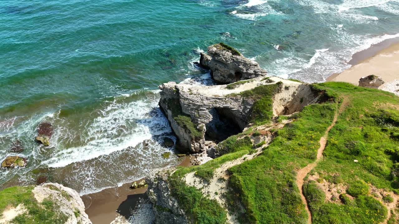 Aerial view of rocky ocean cliffs and calming waves on a sunny day