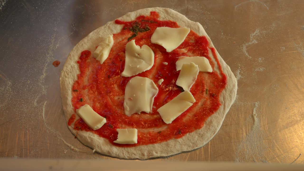 Ripresa dall'alto di uno chef che aggiunge formaggio alla pizza, in una ripresa luminosa, a mezzo primo piano
