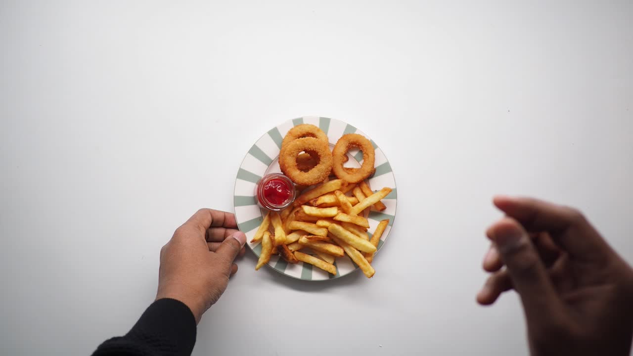Mãos Pegando Batatas Fritas e Anéis de Cebola de um Prato