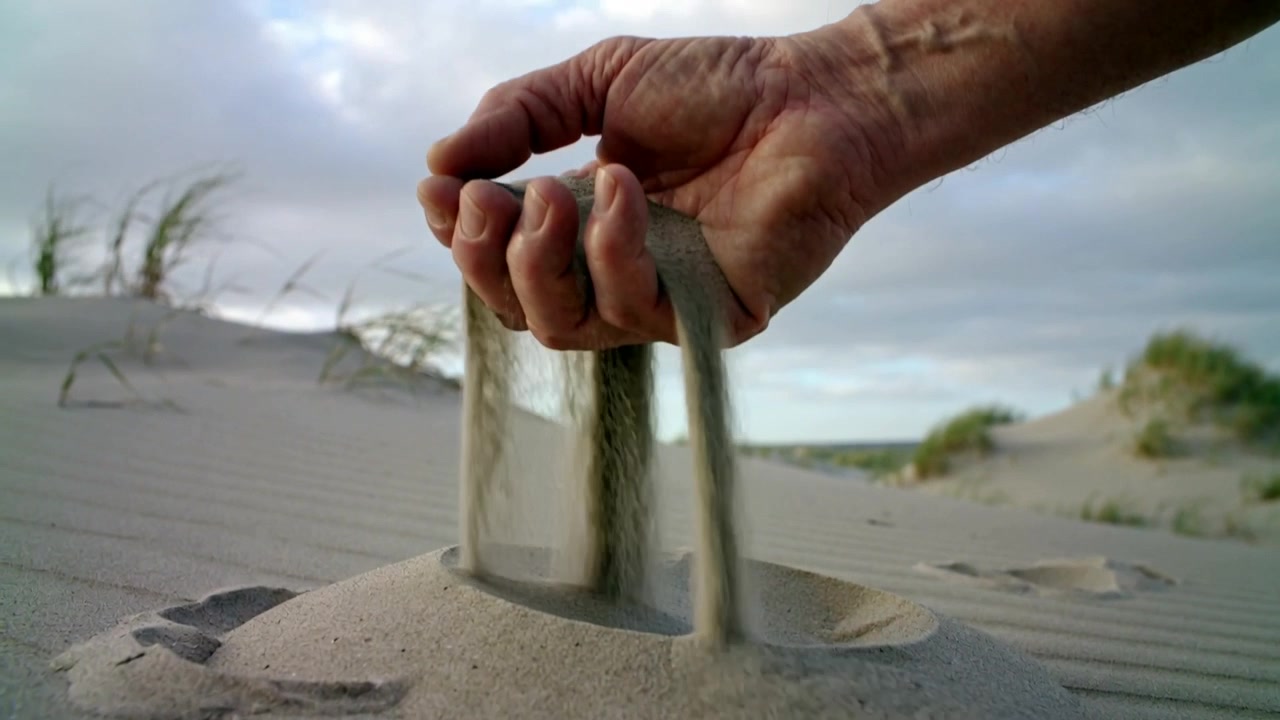Pressing man's hand scooping sand into dome on coastal dune, lifting fingers forming conical pile