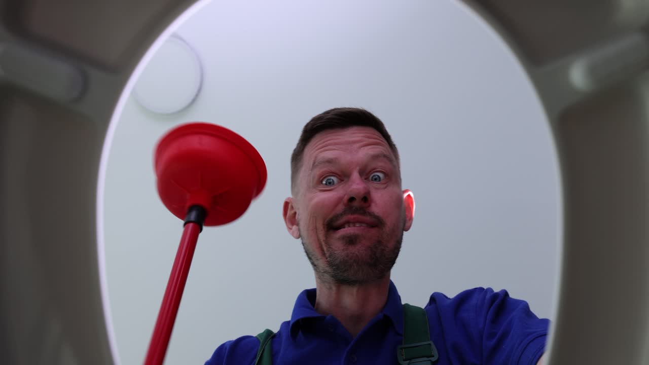 Man looking into a toilet with a plunger