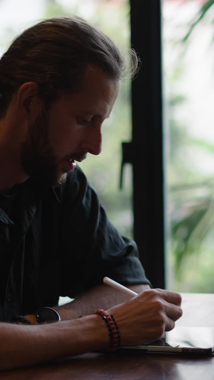 A man creating digital art on a tablet by a window