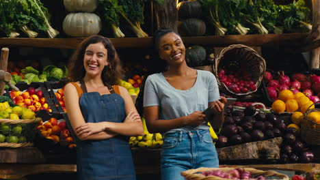 retrato de dos mujeres sonrientes con tableta digital trabajando en un puesto de frutas y verduras frescas en el mercado