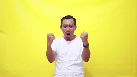 happy asian man celebrating success while raising fists isolated on yellow background