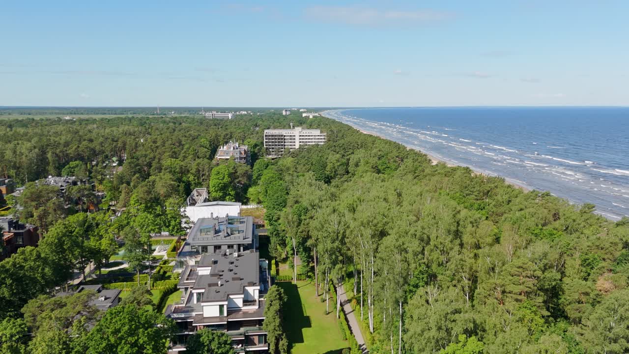 Slow drone pan over Jurmala, Latvia, showing luxury residential villas along the Baltic Sea, bordered by lush pine trees of the Piejūra forest in the Vidzeme region on a sunny summer day
