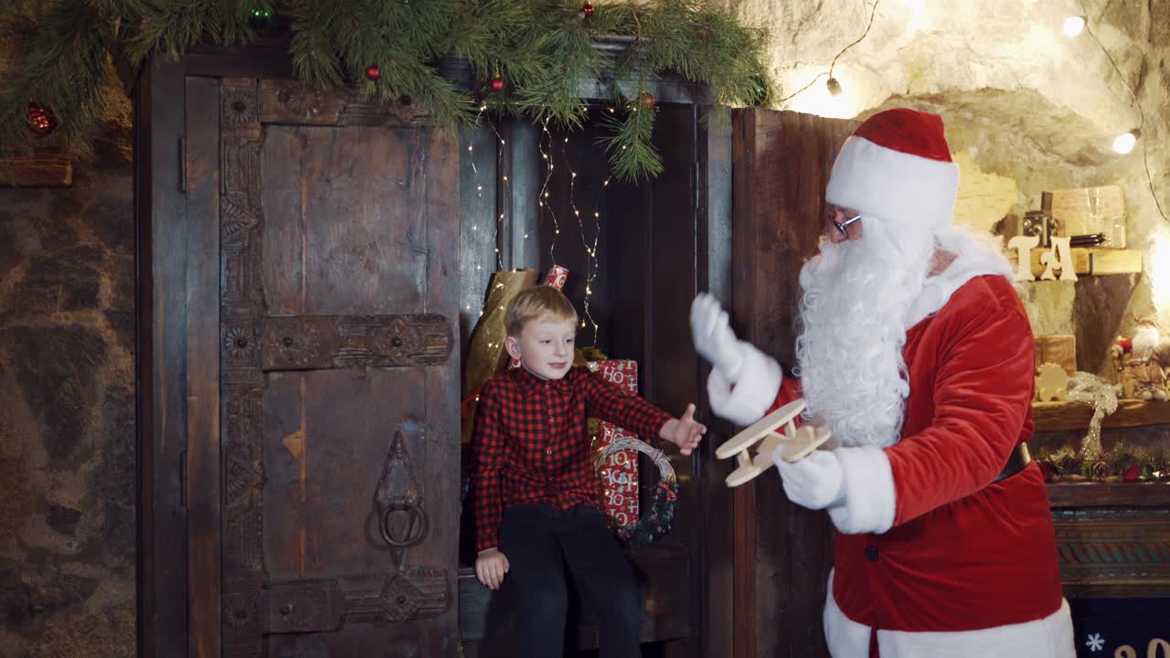 Christmas time. Little boy and Santa Claus with homemade toy plane. Santa shows a happy boy how wooden plane can fly.