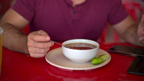 Cierre-En-Cámara-Lenta-De-Un-Hombre-Latino-Revolviendo-Su-Caldo-De-Barbacoa-Con-Una-Cuchara-Y-Dándole-Un-Sorbo-En-Un-Restaurante-En-México