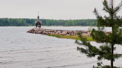 an old chapel stands on a stone promontory on the water in leningrad region russia at cloudy weather, the forest in the background