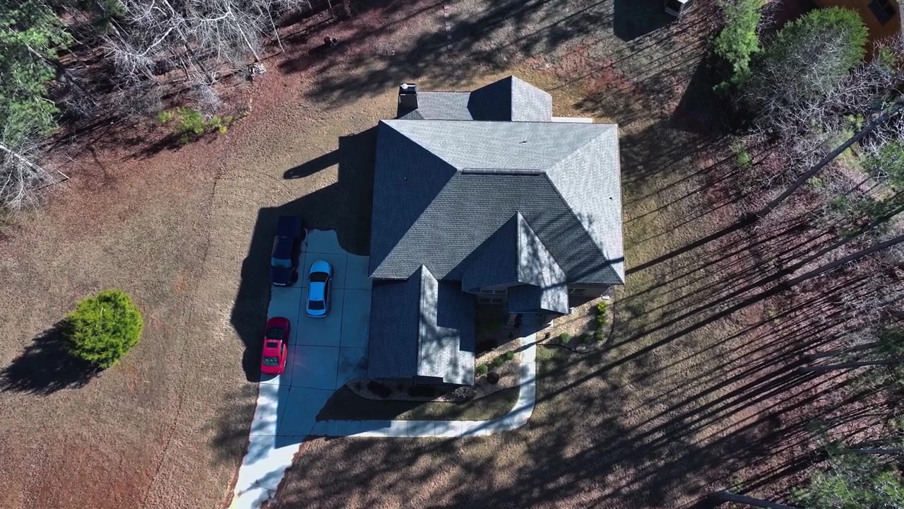 Luxury large single-family home with gray roof, driveway, parked cars, surrounding pine forest and bare deciduous trees under sunny clear sky. Georgia, USA. Aerial top down shot. Sunny summer day.