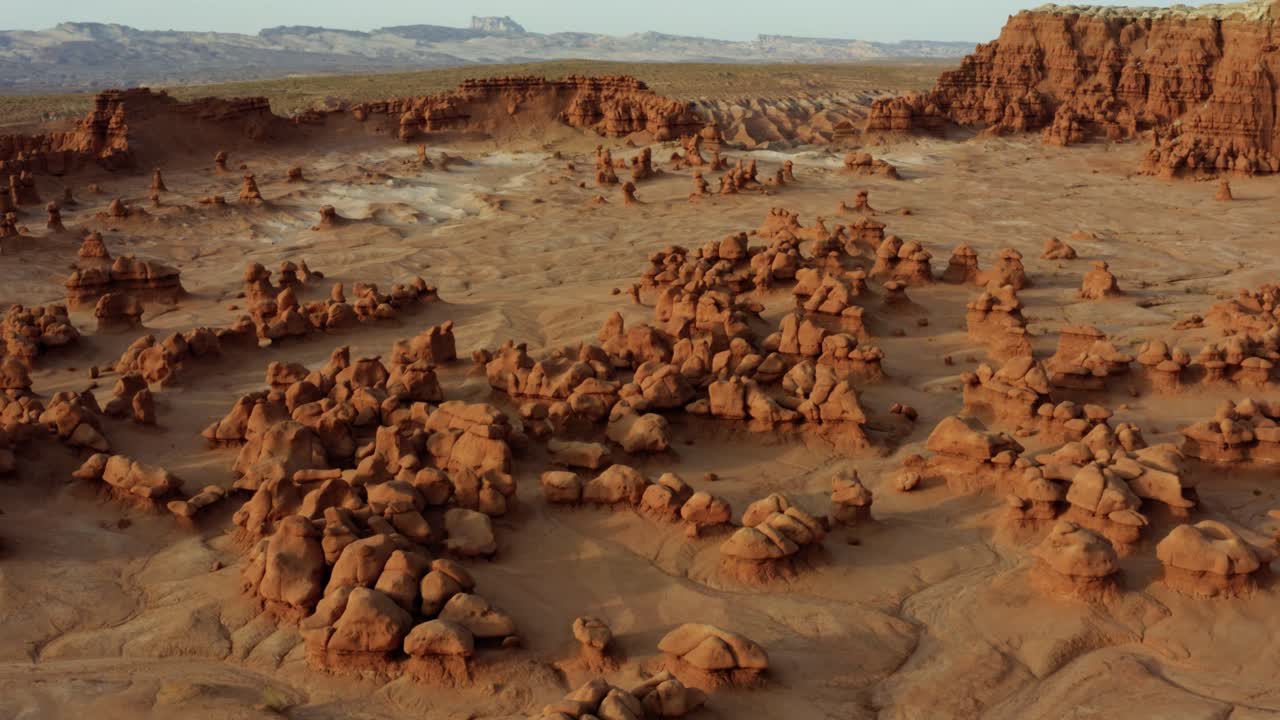 Gorgeous rising and tilting down aerial drone shot of the beautiful Goblin Valley Utah State Park mushroom rock formations with red and white Butte's in the background on a warm sunny summer day