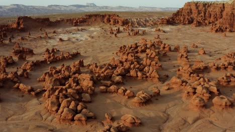 Gorgeous-rising-and-tilting-down-aerial-drone-shot-of-the-beautiful-Goblin-Valley-Utah-State-Park-mushroom-rock-formations-with-red-and-white-Butte's-in-the-background-on-a-warm-sunny-summer-day