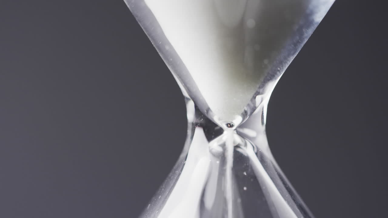 Video of close up of hourglass with sand pouring, copy space on black background