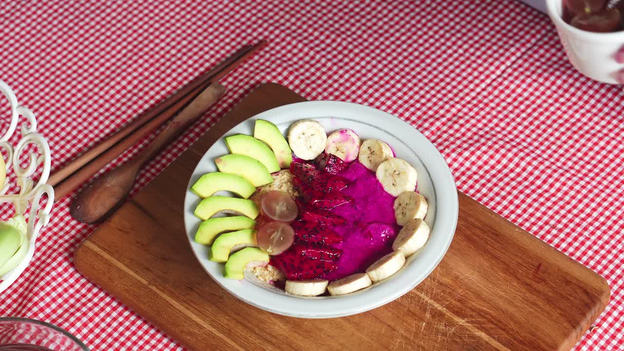 mujer haciendo un tazón de batidos de frutas para la dieta en casa poniendo uvas cortadas
