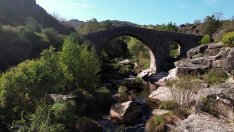 Volando-Sobre-El-Antiguo-Puente-De-Piedra-Sobre-El-Hermoso-Río