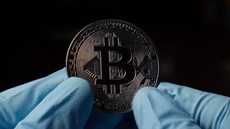 las manos con guantes azules sostienen el símbolo de la moneda criptográfica bitcoin translúcida en fondo negro