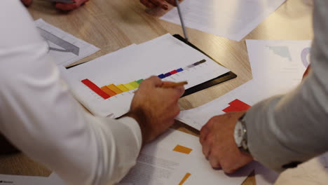 Top-view-of-multiethnic-people-hands-with-pencils-analyzing-documents,-charts,-financial-reports-and-graphics-on-white-wooden-table