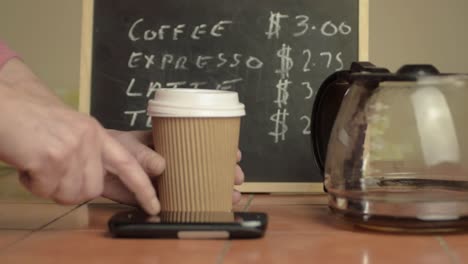 hands holding a takeaway coffee to-go with cellphone close up