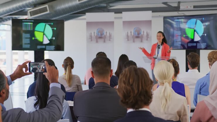 Uomo tra il pubblico a una conferenza aziendale che filma con lo smartphone