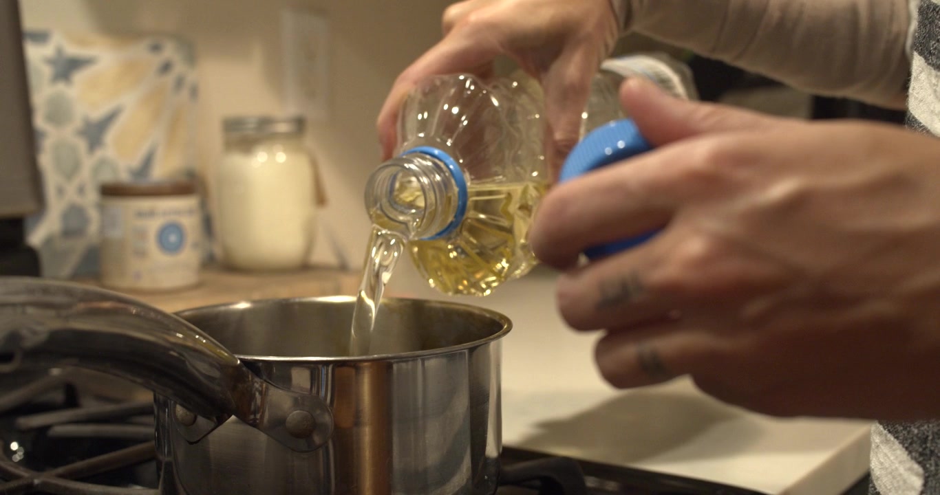 Óleo de cozinha é despejado em uma panela antes de fazer pão frito caseiro. Close-up de um processo de preparo de alimentos em cozinha doméstica, destacando a culinária tradicional e as rotinas culinárias diárias.
