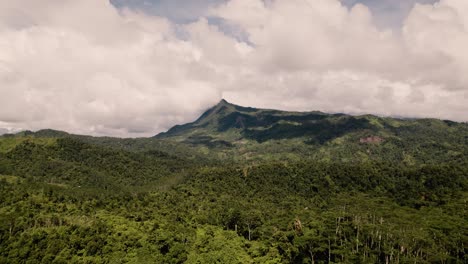 Aerial-drone-shot-while-hiking-deep-in-the-jungels-in-Davao,-Philippines-on-a-warm-sunny-day-and-lush-green-palm-trees-and-different-mountain-peaks-with-layers-and-shadow-driving-a-curvy-road