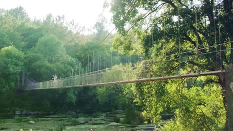 scenic suspension bridge over river in lush forest, man vlogging outdoors