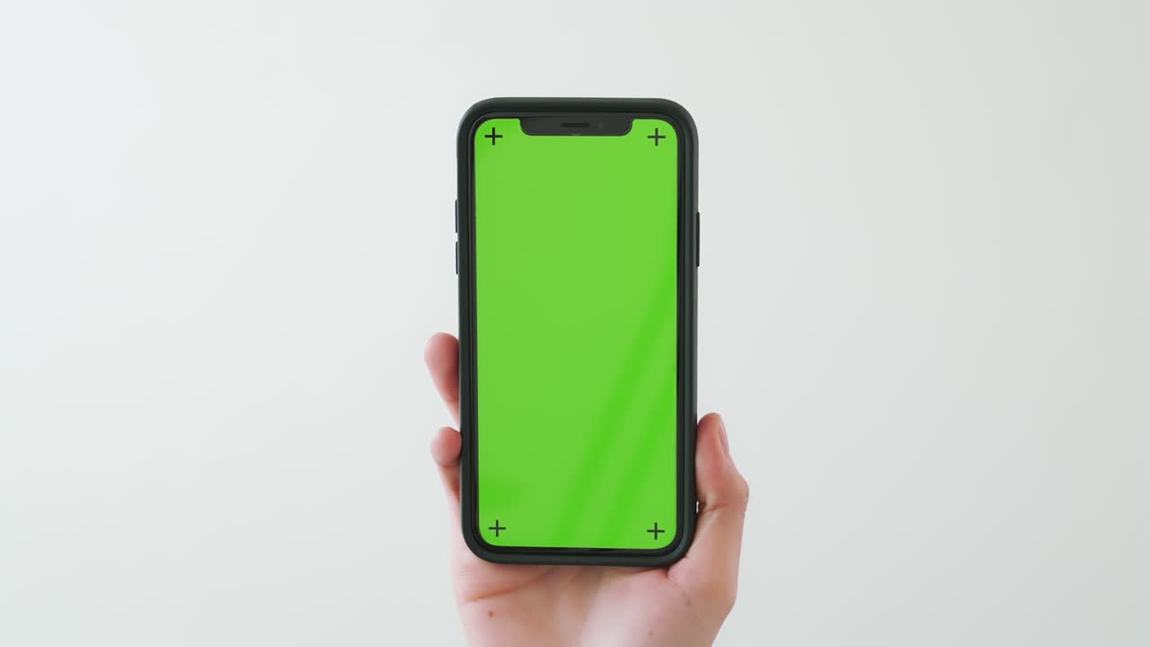 Mano che tiene uno smartphone con schermo chroma key e lo mostra su sfondo bianco.