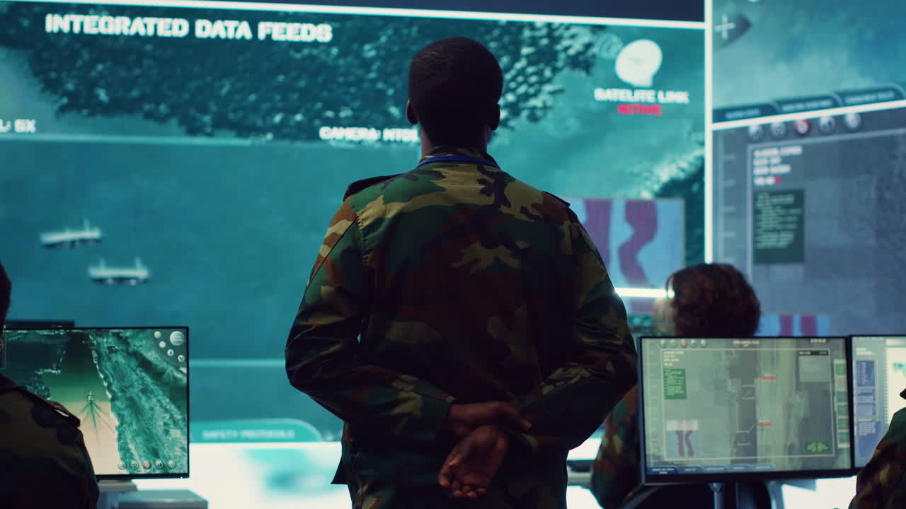 Oficial del ejército examinando imágenes de vigilancia por satélite en una gran pantalla