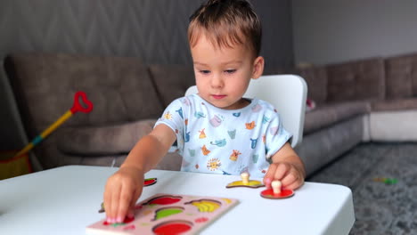 adorable caucasian baby boy studying through the game. toddler plays at desk and collecting fruit puzzles.
