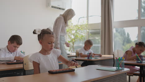 el maestro camina por el aula de la escuela. un grupo de niños está sentado en sus escritorios. los niños escriben la tarea. una lección de la escuela primaria en cámara lenta. realizar un trabajo de control